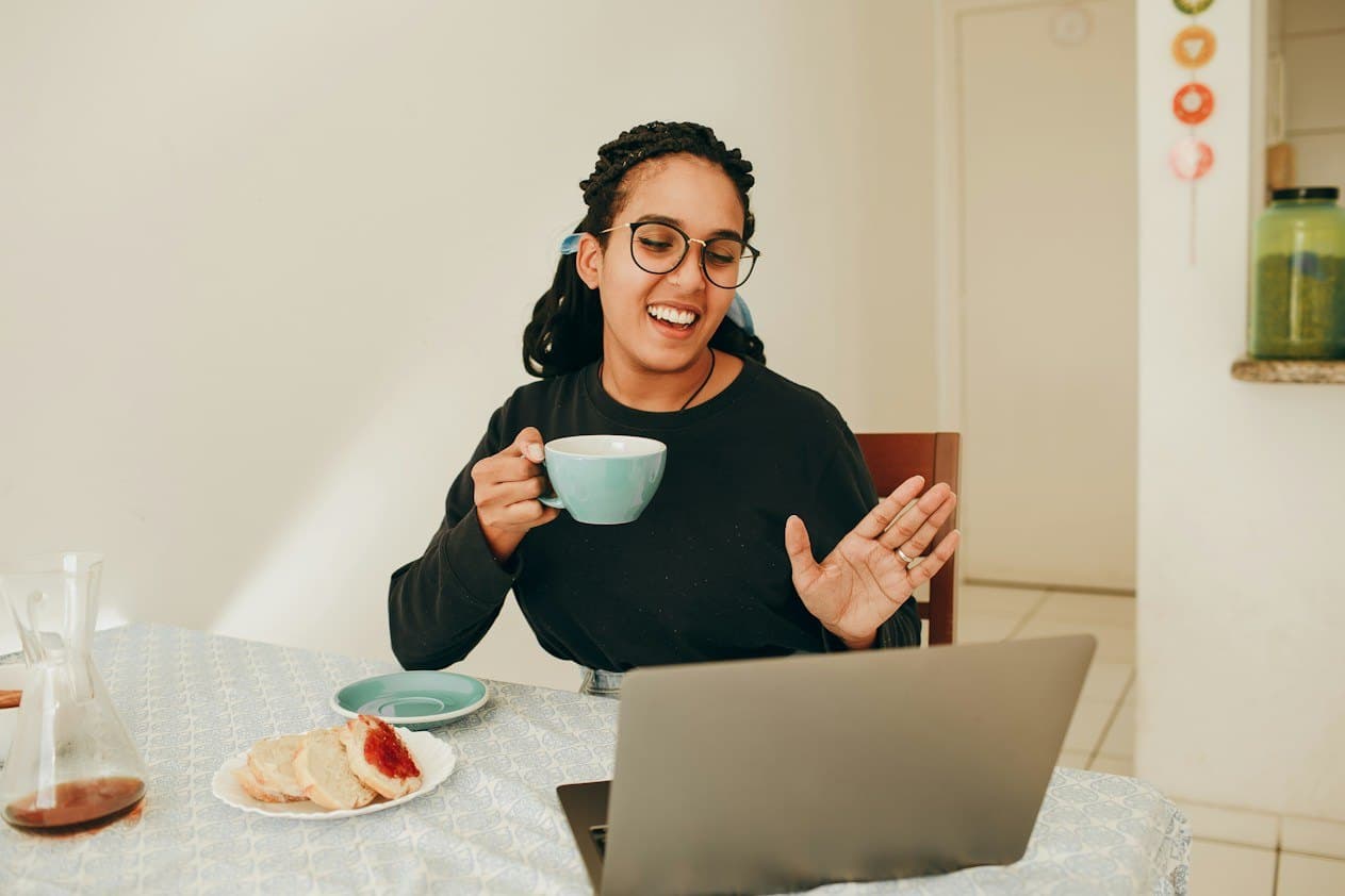 Smiling woman with a cup of tea on a video call at her laptop