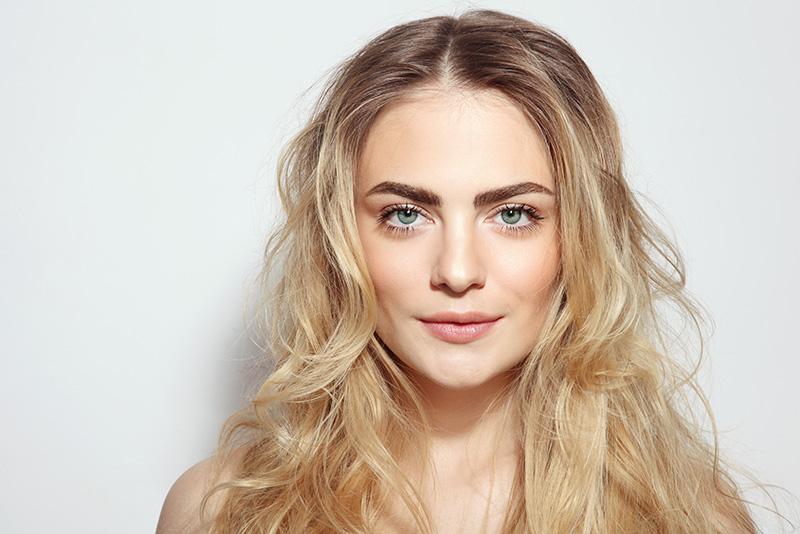 Close-up of a young woman with long blonde hair and clear skin, representing the benefits of ResurFX skin resurfacing treatments offered by Dr. Monika Kiripolsky.